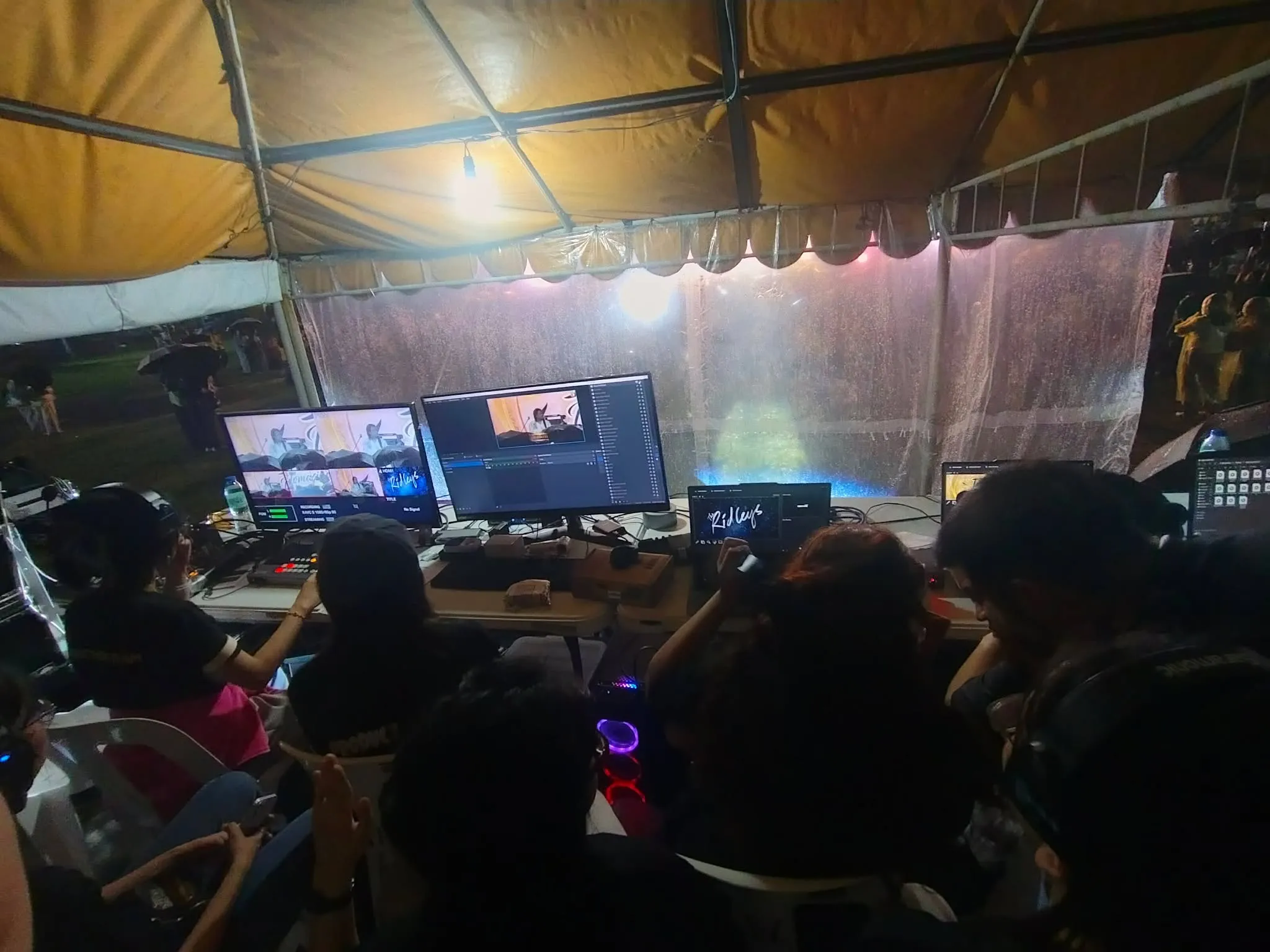 The production tables under the tent, monitors lit and the crew at work.