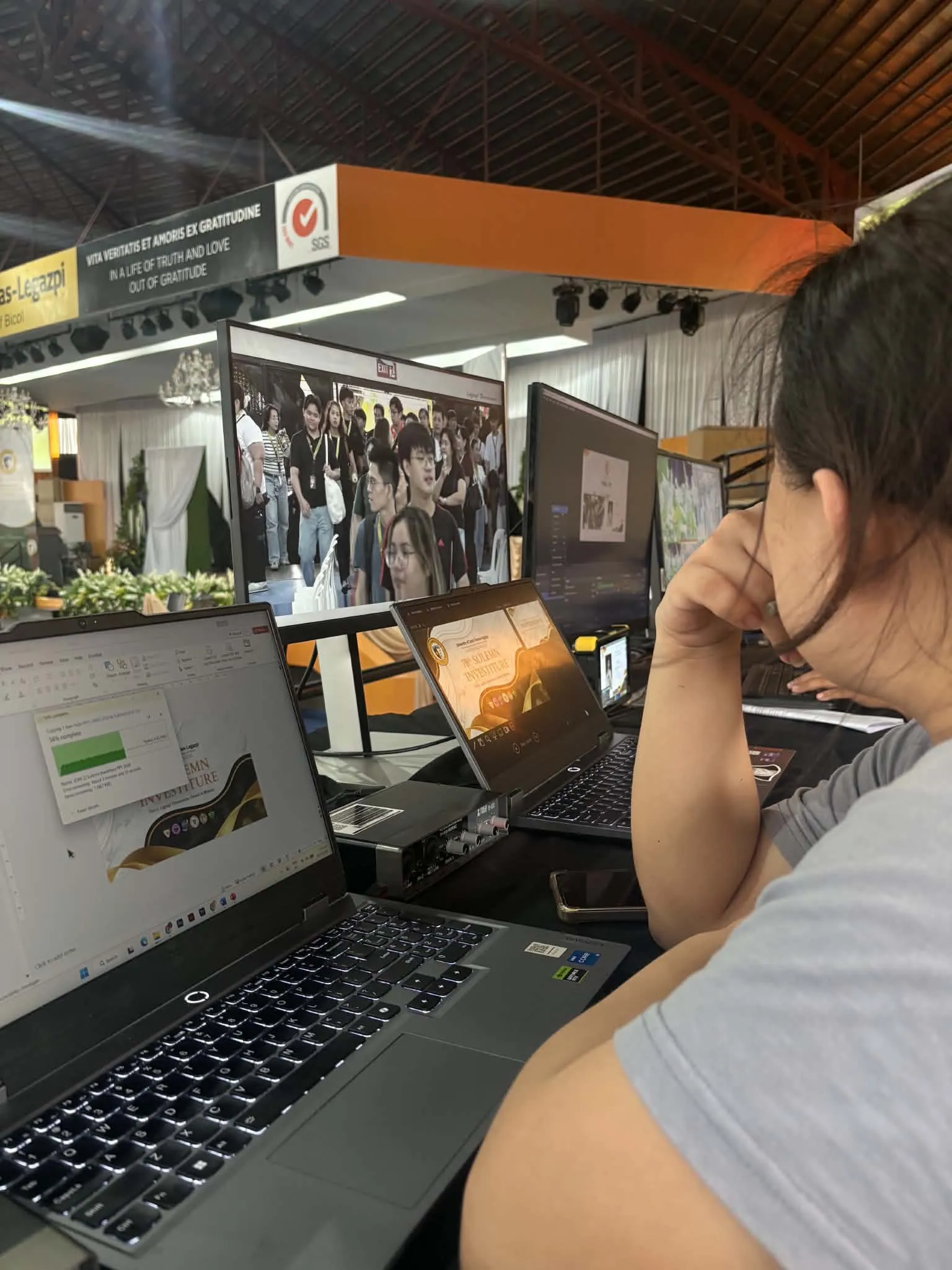 A crew member at a laptop beside the stage during a year-end program.