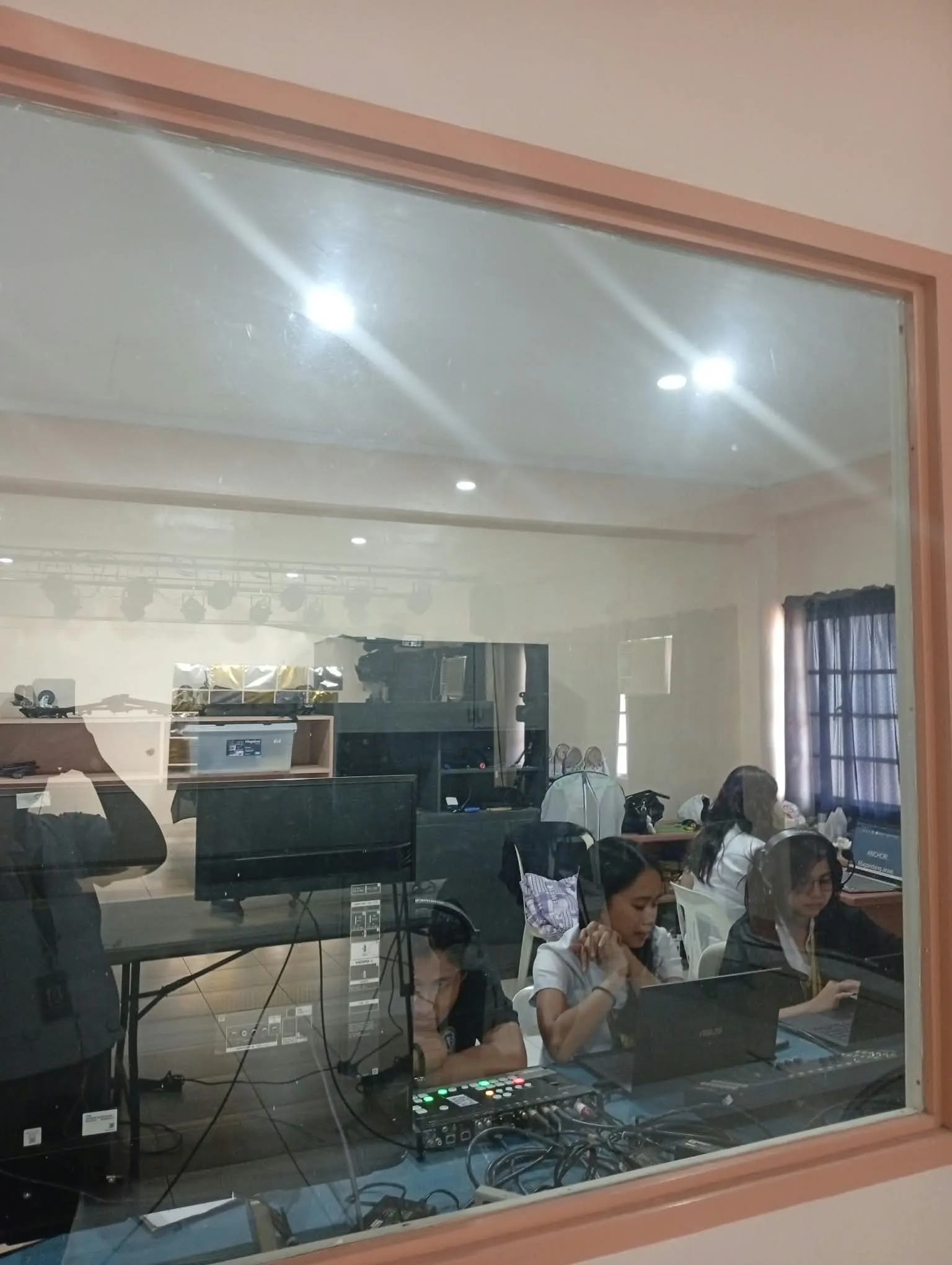 Students at work in a production room, seen through a glass window.
