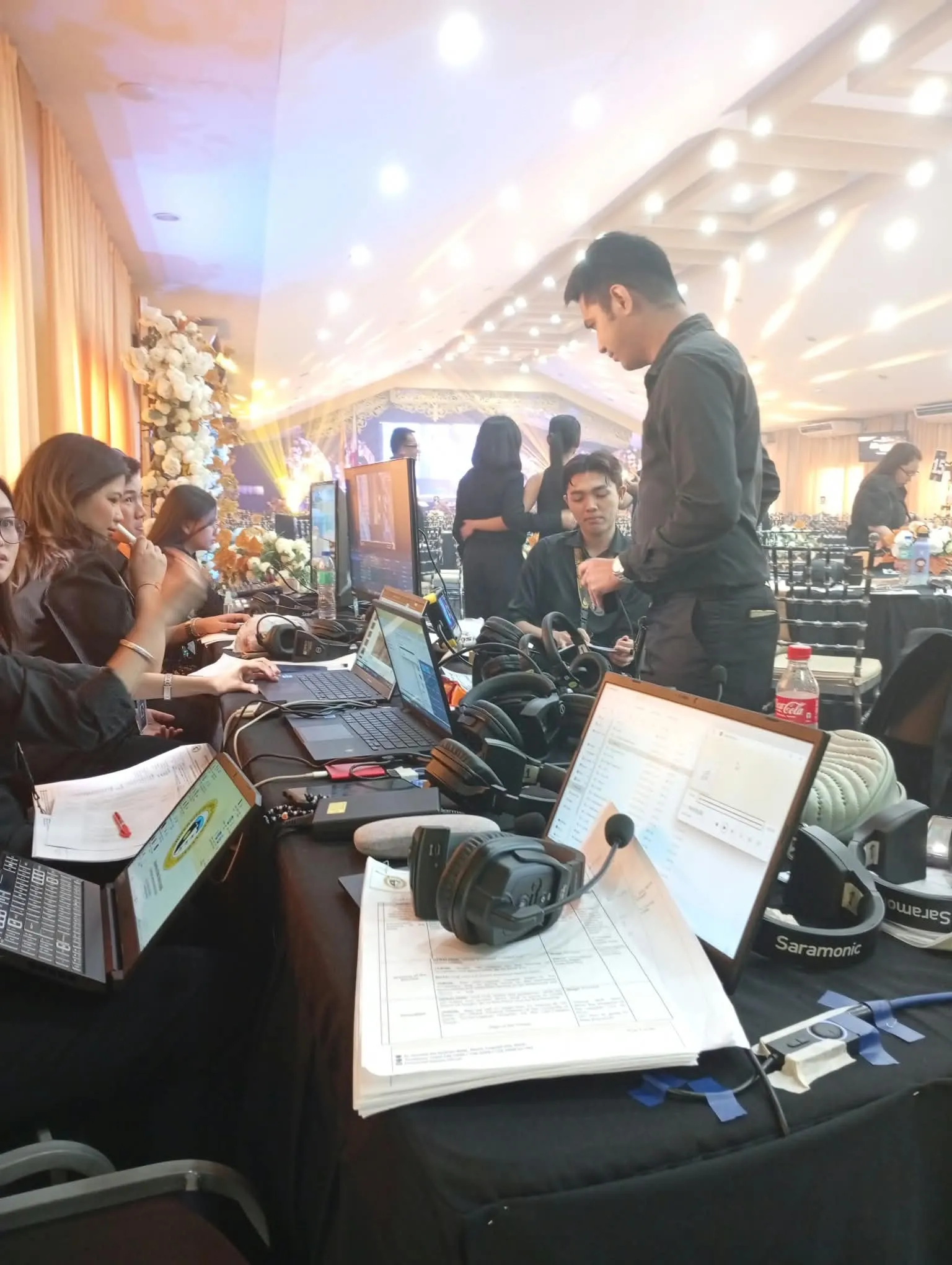 The production desk in the ballroom, laptops and headsets set out as the crew works.