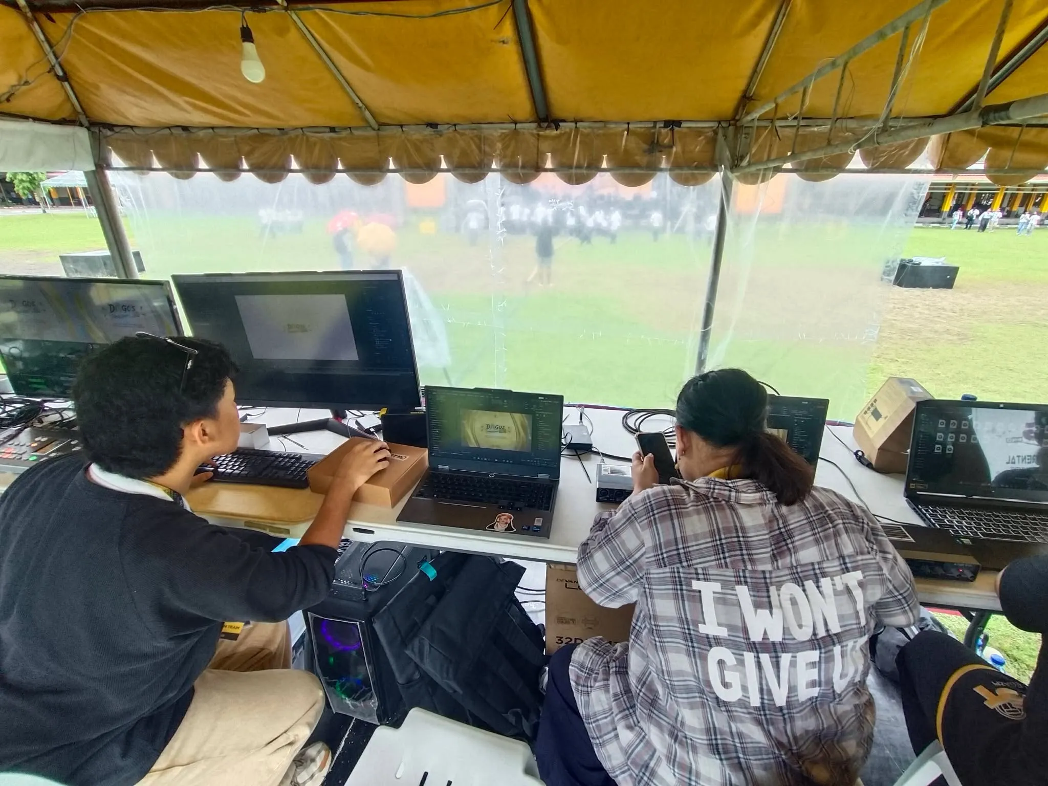 Two crew members at laptops under the production tent.