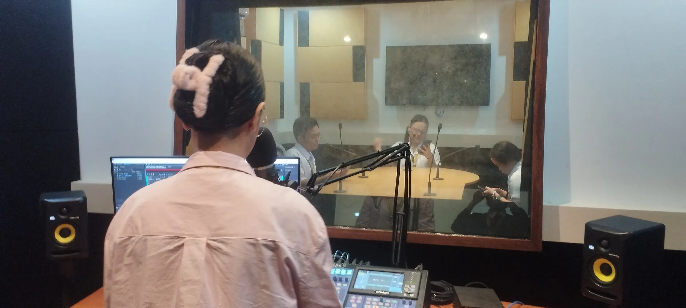 A student at the studio window behind a microphone arm.