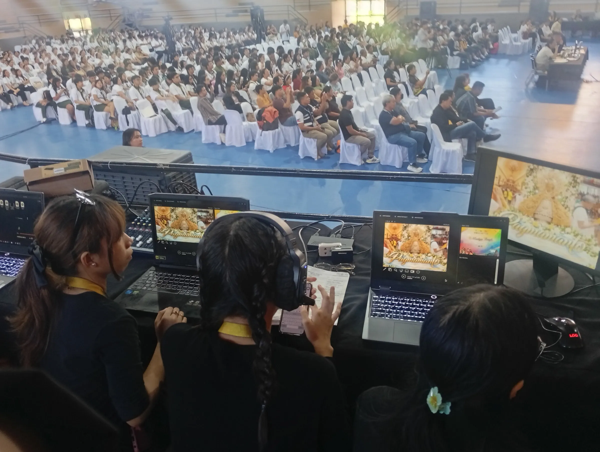 Crew at laptops facing the packed gym.