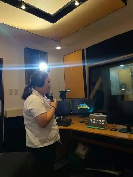 A host at the microphone in the studio, the wall timer behind.