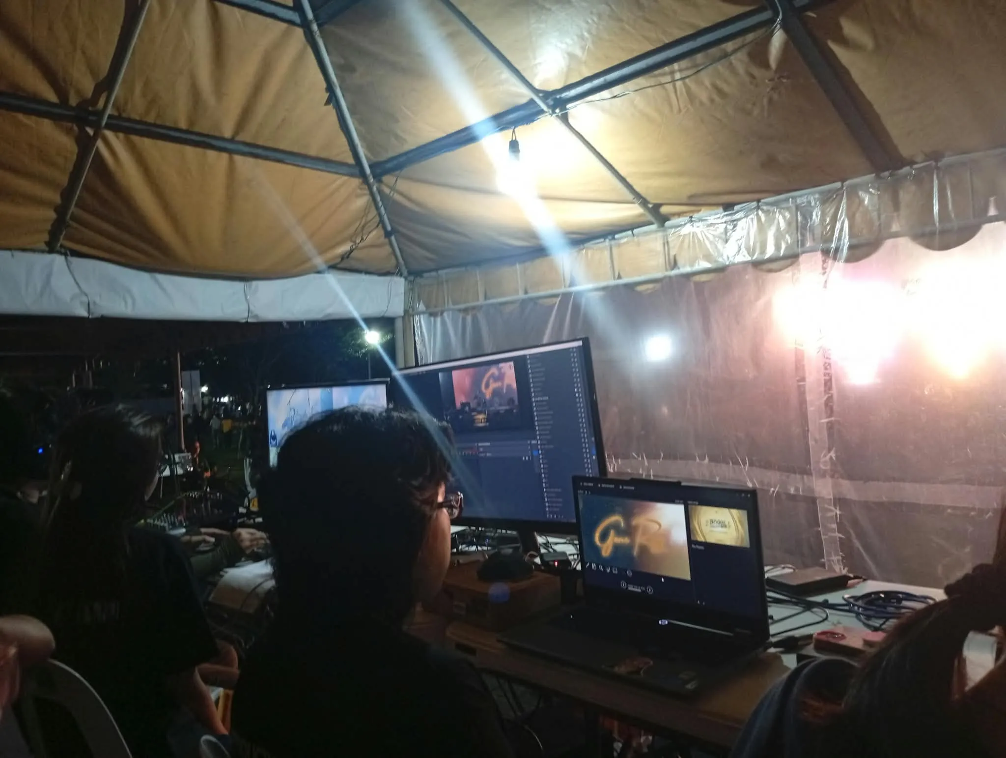A crew member at the laptops and monitors under the production tent at night.