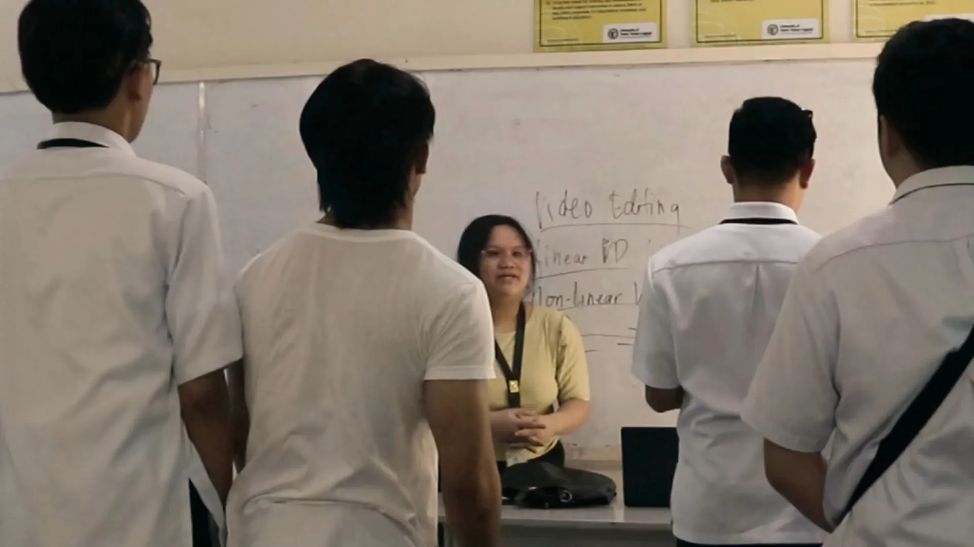 A still from Padayon, Christine in character at a classroom desk, surrounded by students.