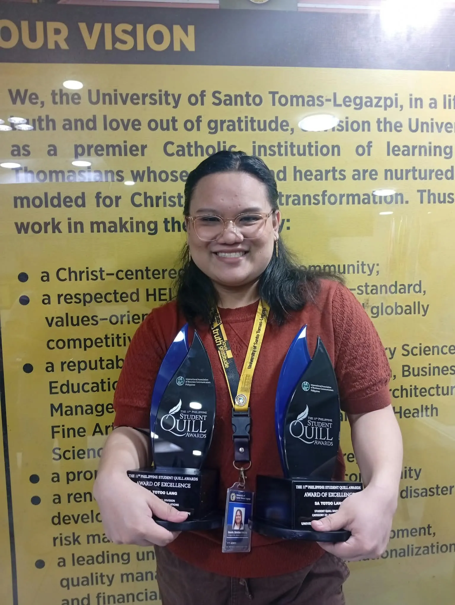 Christine holding two Quill trophies in front of the university’s vision statement.